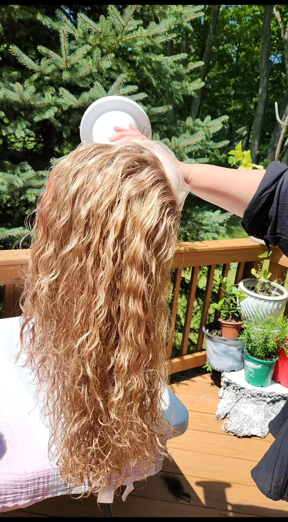 A long curly blonde wig on a head form being styled outdoors